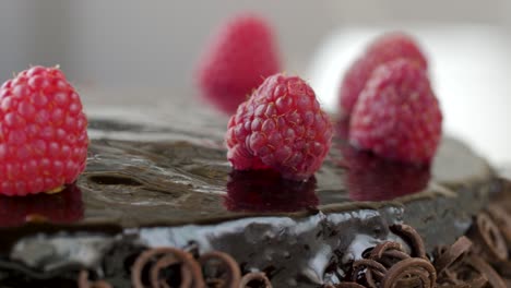 close up shot of chocolate cake topped with raspberries and garnished chocolate spirals rotating counterclockwise