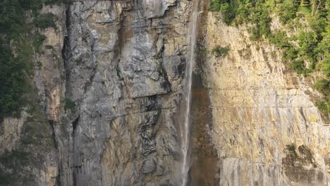 Drone-shot-of-Seerenbachfälle,-powerful-waterfall-flows-over-rockes,-surrounded-by-lush-green-trees,-Amden-Betlis,-Walensee,-Switzerland