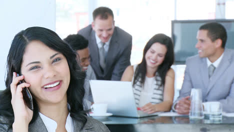 Mujer-De-Negocios-Hablando-Por-Teléfono-Con-Su-Equipo-Trabajando-En-Segundo-Plano