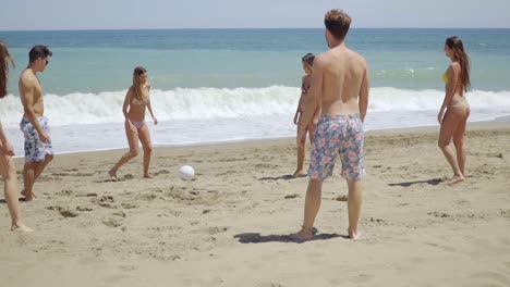 Grupo-De-Amigos-Pateando-La-Pelota-En-La-Playa-Soleada