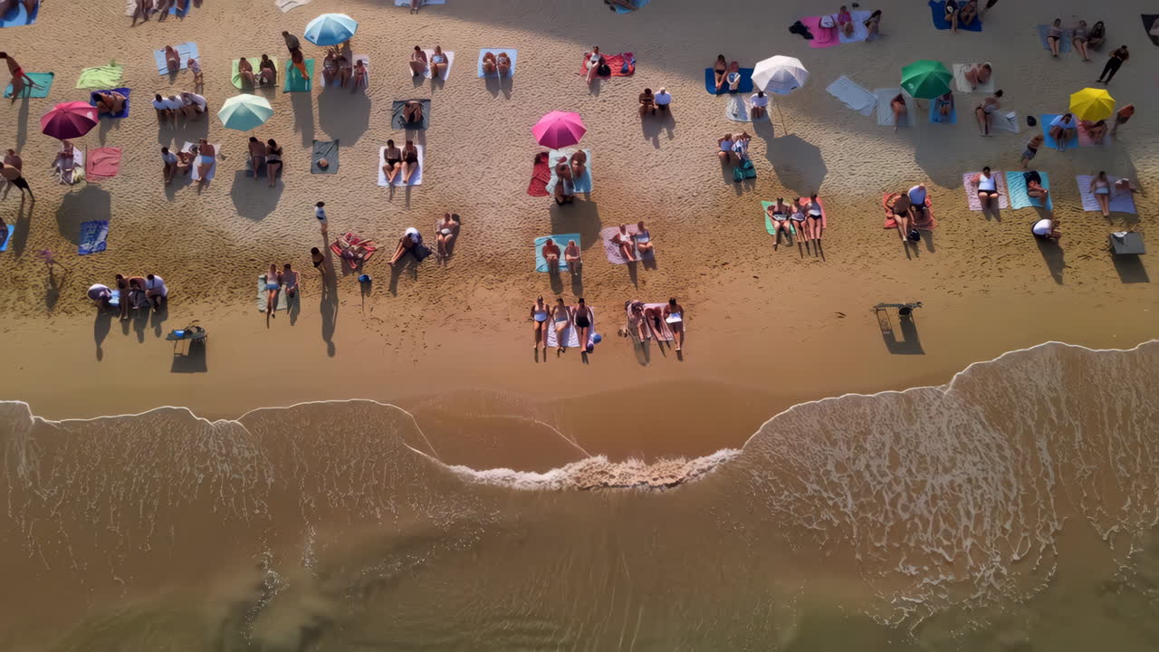 Aerial View of a Crowded Beach with People, Umbrellas, and Ocean Waves