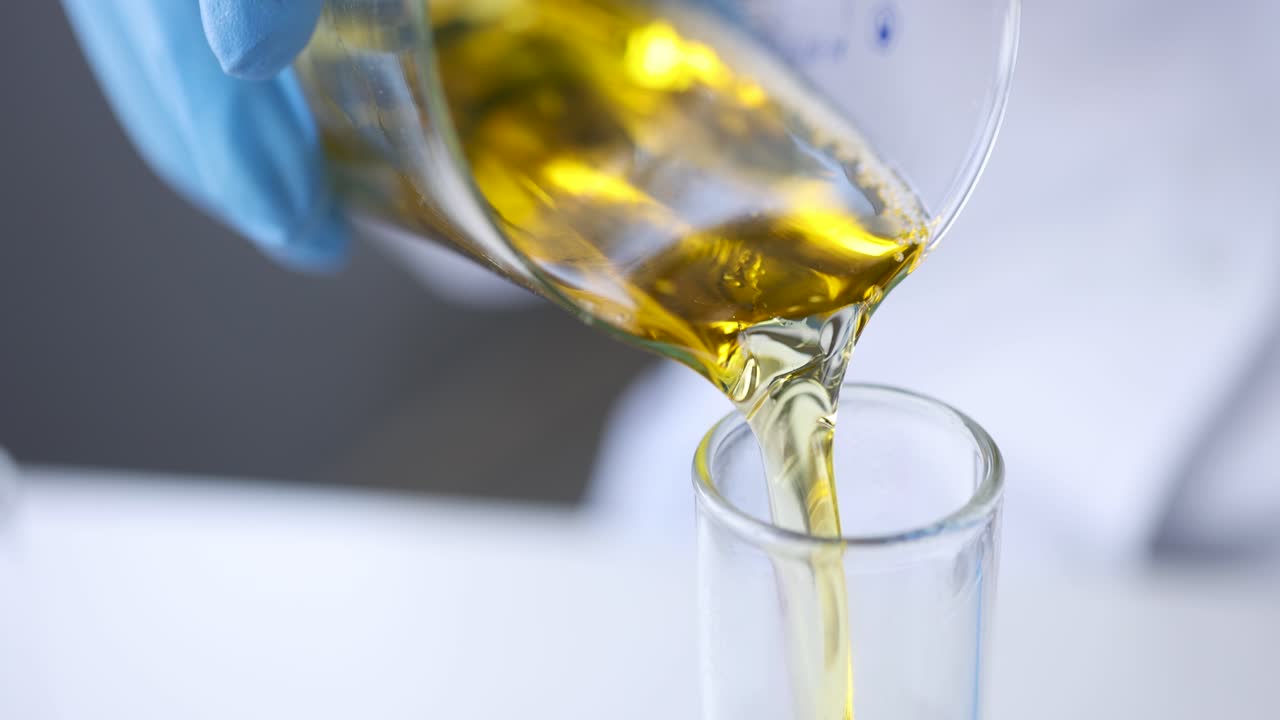 Scienziato chimico che versa liquido giallo da un bicchiere in una provetta, filmato 4k