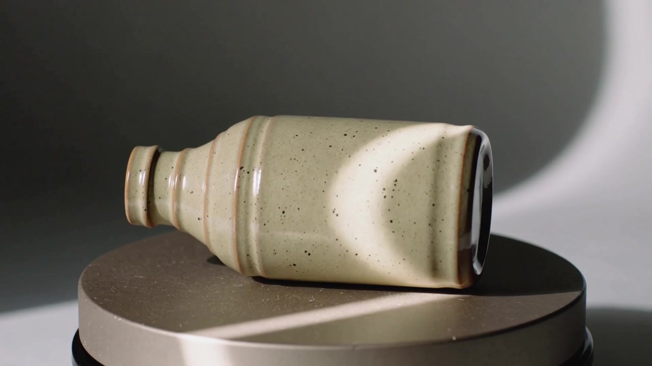 Rotating speckled ceramic bottle on studio turntable as motor starts, revealing glossy glaze lit