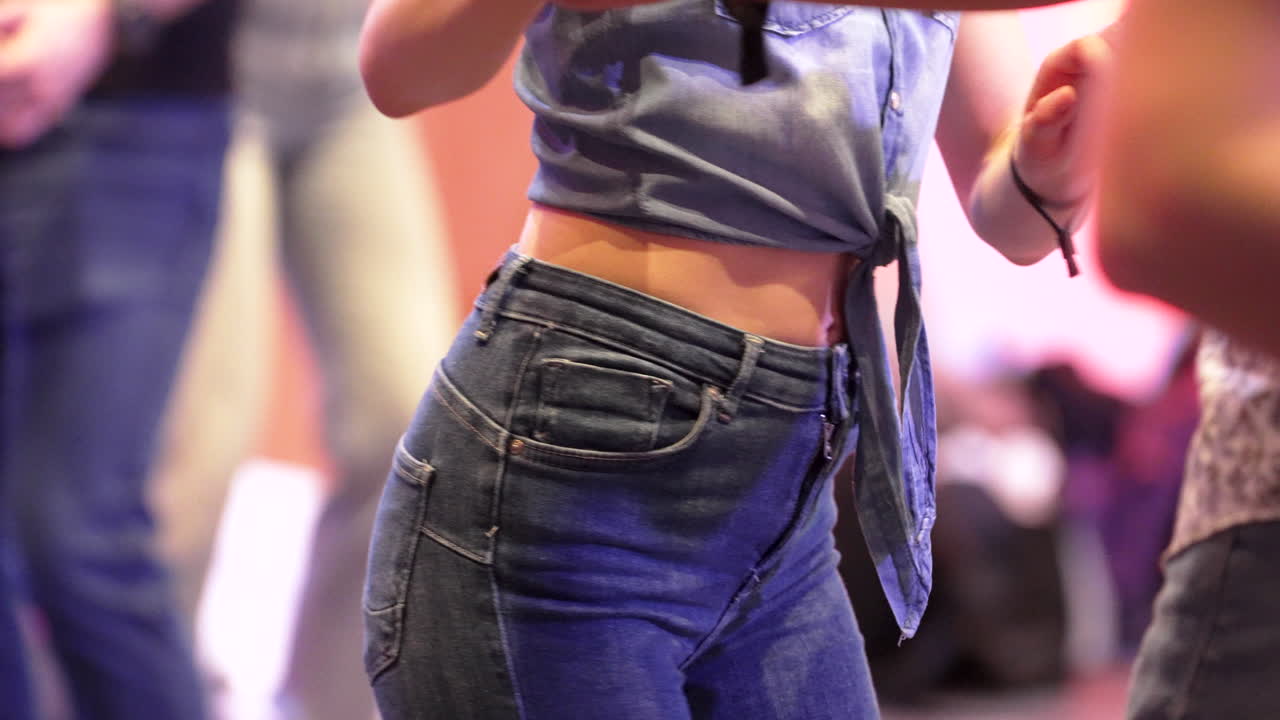 Slow motion salsa dance by a woman wearing knotted shirt and blue jeans
