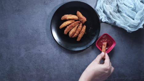 hand holding a crispy fried potato wedge with tomato sauce