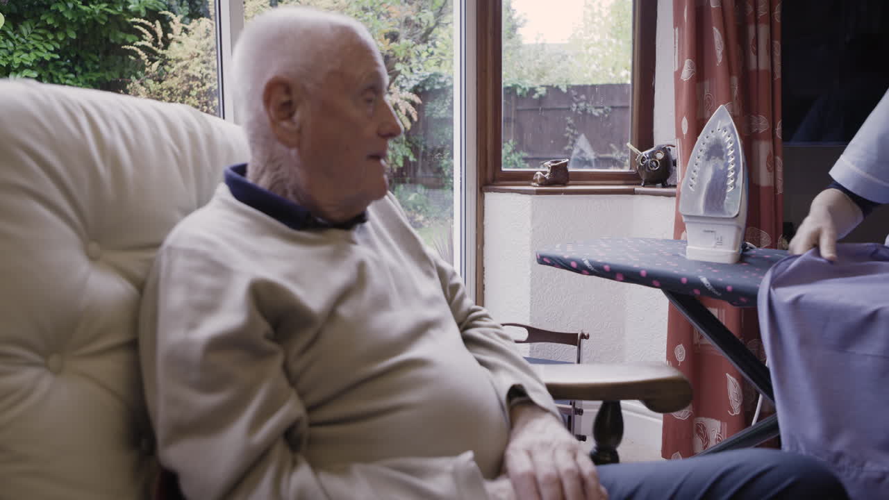 Caregiver assisting elderly man with ironing at home