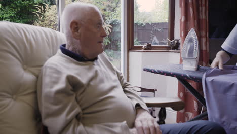 caregiver assisting elderly man with ironing at home
