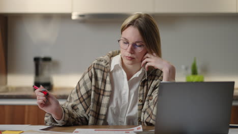 Eine-Frau-Mit-Brille,-Die-An-Ihrem-Arbeitsplatz-Mit-Einer-Laptop-Anwendung-An-Finanzdokumenten-Arbeitet-Und-An-Ihrem-Arbeitsplatz-Sitzt,-Sieht-Konzentriert-Aus-Und-Erledigt-An-Einem-Fruchtbaren-Arbeitstag-Eine-Aufgabe-Und-Bereitet-Die-Prüfung-Eines-Berichts-Vor.