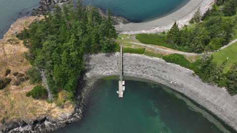 high up aerial shot of a lone dock extending out onto a shallow cove of water on whidbey island