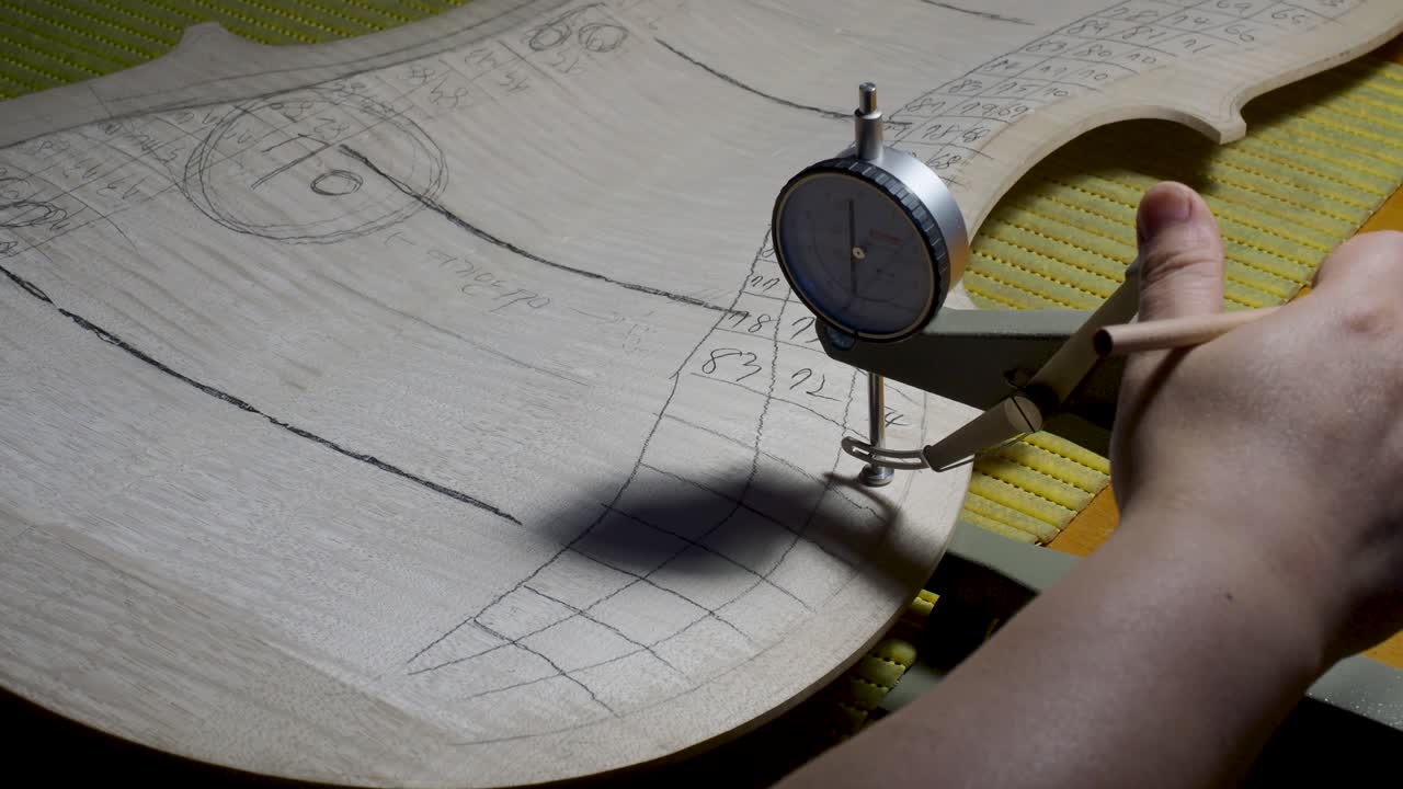 fabricante de instrumentos de cuerda maestro luthier proceder con el trabajo de graduación en la placa trasera del violonchelo, usar calibre medidor de grosor, medir niveles, usar lápiz escribir valores en madera, taller de cremona, italia