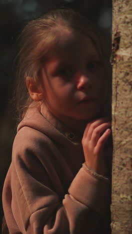 lonely child leans on tree trunk in dark forest. little girl lost in night nature park during travel. kid threatened by darkness and sounds in wild wood