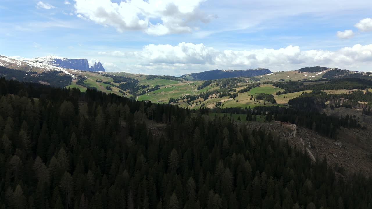 imágenes de drones en timelapse volando a través de seiser alm, mostrando prados ondulados, bosques y la montaña schlern bajo un cielo dinámico