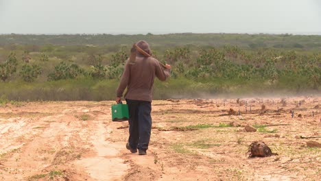 a farmer walks across a dry dusty crop field carrying his tools