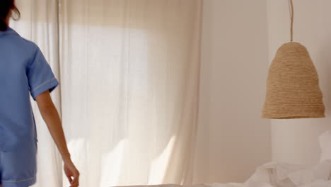 woman in pajamas opening curtains, enjoying morning sunlight at home