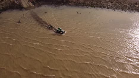 Aerial-tracking-shot-of-tractor-entering-lake-during-sunny-day,-4K