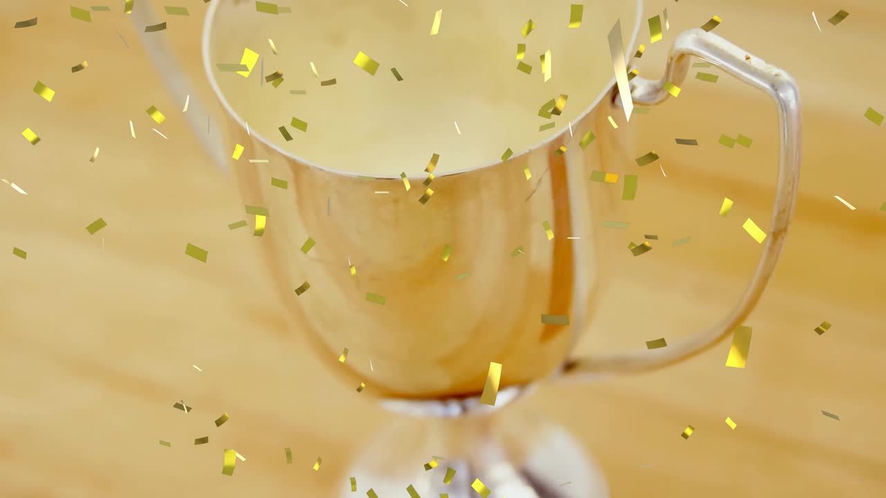 Gold confetti falling and swirling around silver trophy cup creating celebration on wood tabletop