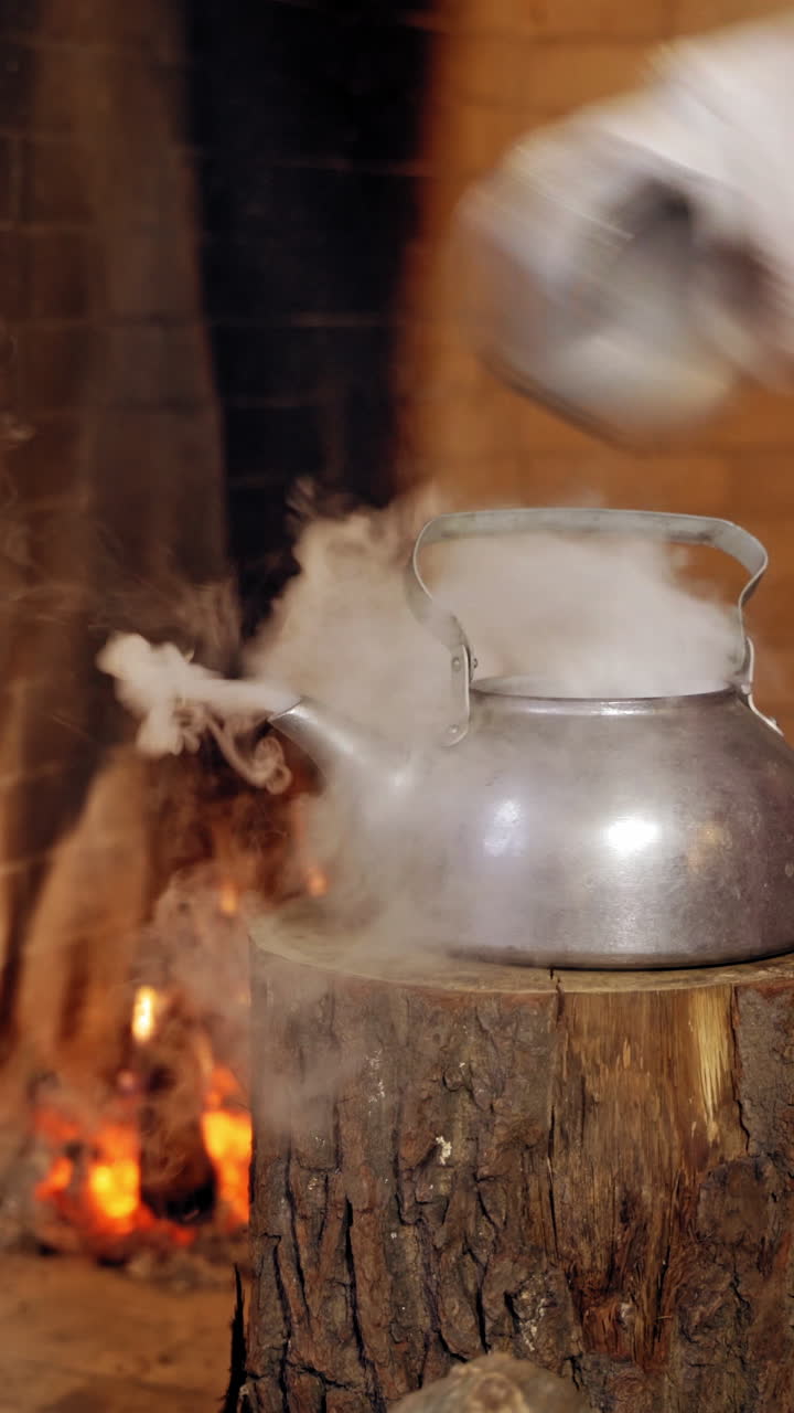 Boiling retro aluminium kettle. Teapot steams. Santa Claus takes a boiling kettle. Closeup. Teapot on a log. Vertical video