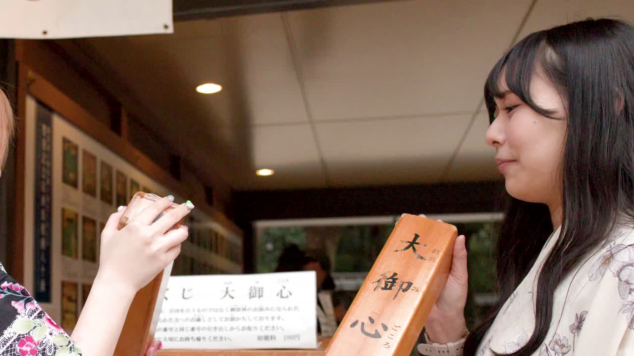 Uma mulher japonesa vestindo um quimono tradicional agita uma caixa de sorte de madeira em um santuário.