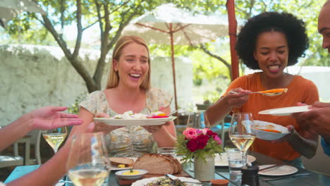 group of friends enjoying outdoor meal and wine on visit to vineyard restaurant