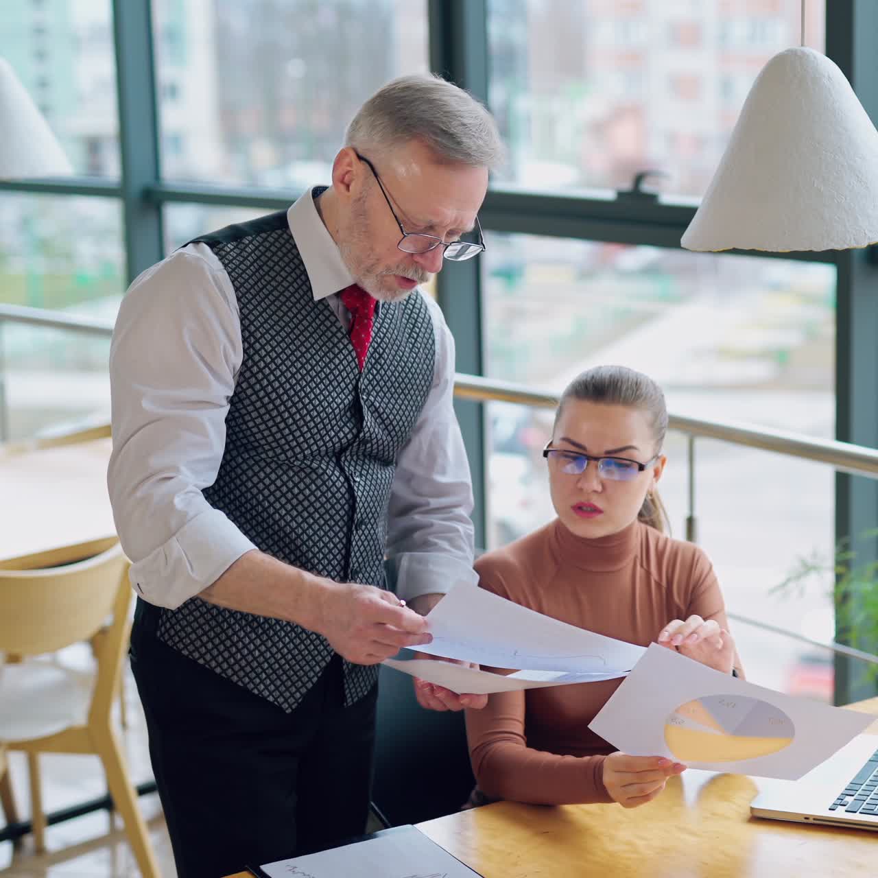 Young woman talks to her boss indoors. Grey-haired businessman discuss project works with his secretary in the office.