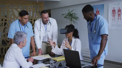 asian female doctor at table using vr headset with a diverse group of colleagues gathered around her