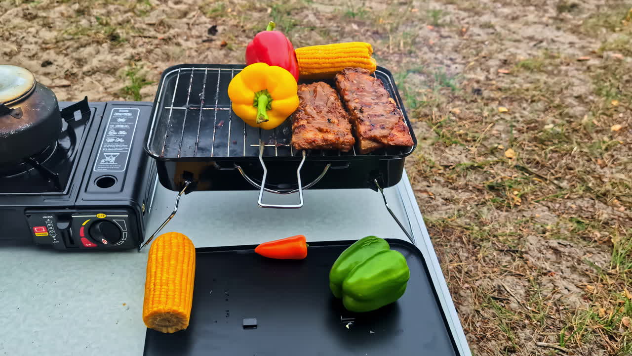 Grilled ribs and vegetables cooking on portable stove at picnic on a seaside