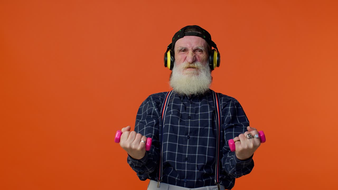 Äldre skäggig man lyssnar på musik via hörlurar, tränar och lyfter rosa hantlar, friskvård.