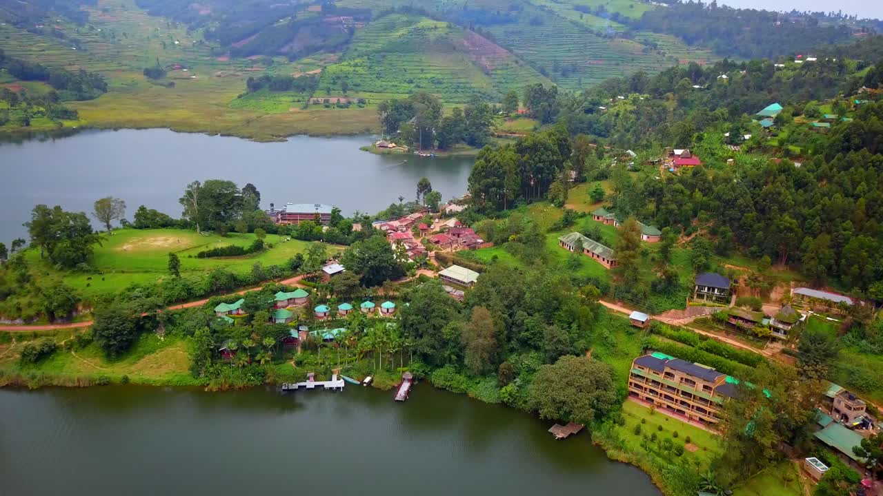 Luchtfoto van lodges aan het meer en aanlegsteigers bij Rutinda aan het Bunyonyi-meer, Oeganda, met het Lake Bunyonyi Rock Resort en andere toeristische accommodaties genesteld in weelderige heuvels