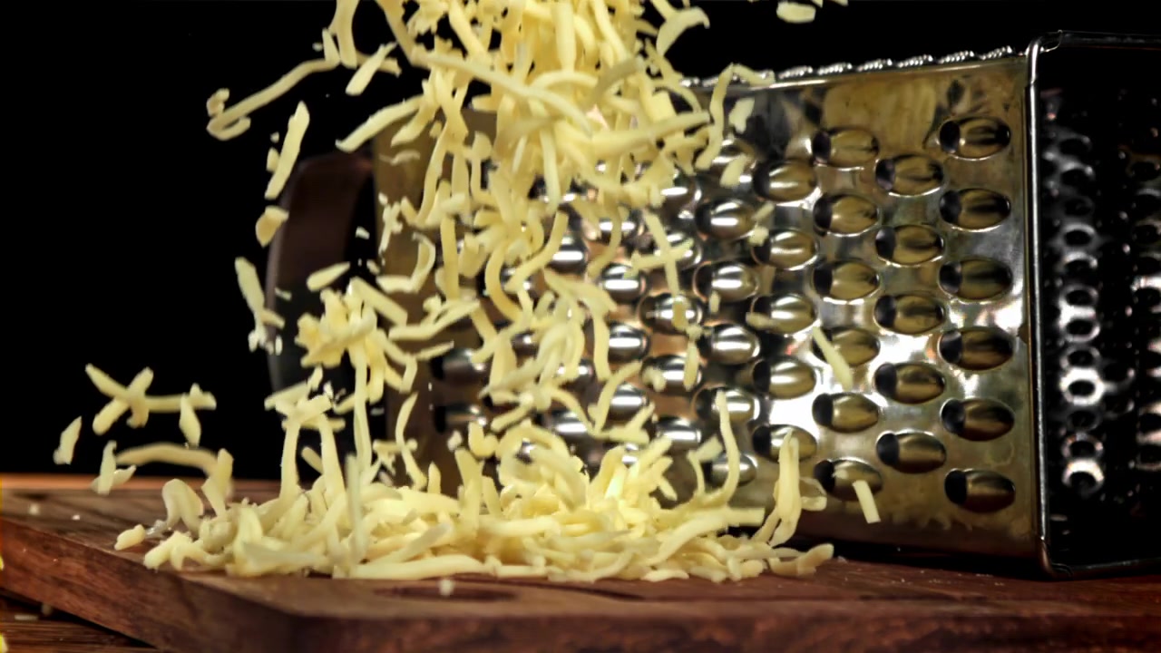 Formaggio grattugiato fresco che cade su un tagliere di legno al rallentatore