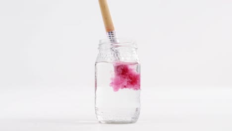 close-up of paintbrush with pink paint being washed in water