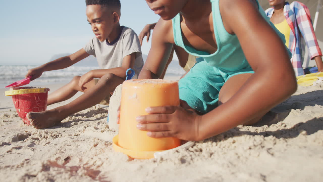 Afroamerikanskt syskonpar leker med sand på stranden.