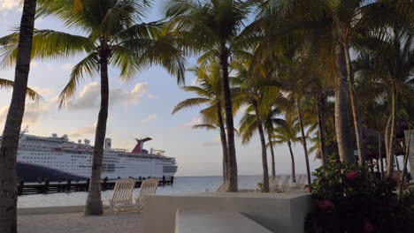 golden sky with palm tries to cruise ships in backgrounds, no people, paradise look. lounge chairs and white sand.