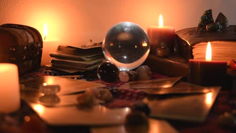 background of a fortune teller table covered with fabric, with crystal balls, stones, matches, cards, ancient books, rings and candles with flickering flames