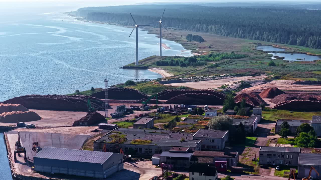 Coastal wind turbines spinning near industrial port with barges and shoreline
