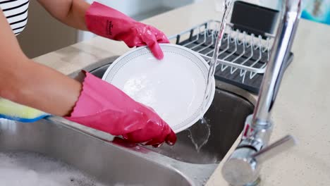 person wearing pink gloves washes dishes under running water in a modern kitchen sink