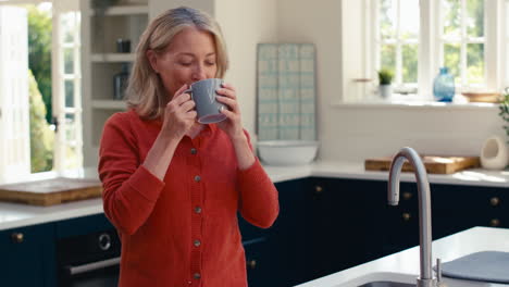 Lächelnde-Reife-Frau,-Die-In-Der-Küche-Steht-Und-Sich-Bei-Einer-Tasse-Kaffee-Entspannt