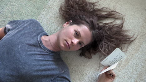 a woman lays on a soft white carpet, holding a love letter and gazing into the camera as it slowly circles around her, creating an intimate, emotional moment of reflection and romance.