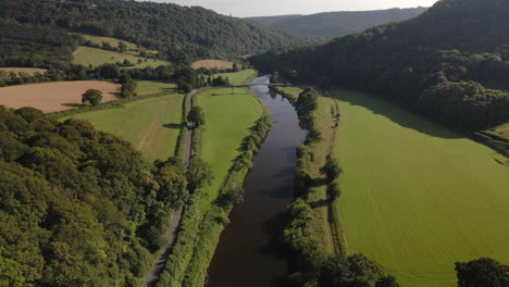 slow moving aerial footage of river wye surrounded by lush green fields and historic woodland on bright summers day