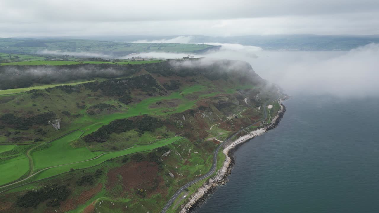 북아일랜드의 글렌아름 마을 근처의 바위 해안 도로 위에서 올라오는 공중 촬영. 푸른 바다, 멋진 초록색 풍경과 바위와 함께 바다 해안의 전망