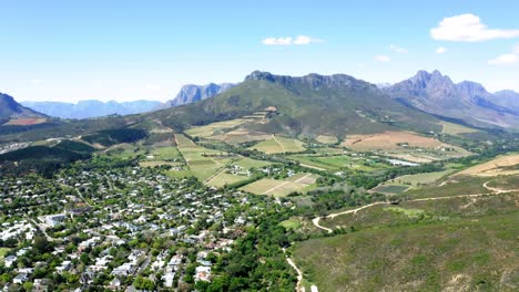 Aerial-of-suburban-neighbourhood-and-farms-in-green-valley-between-mountains,-Stellenbosch,-Coetsenburg-and-Jonkershoek-area