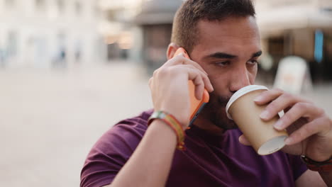 un joven tiene una llamada mientras bebe café al aire libre.