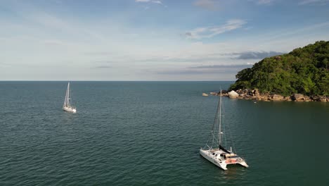 aerial shot of boat and yacht cruising near a rocky island with crystal clear water