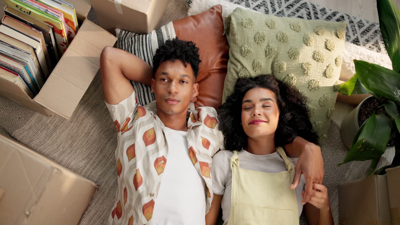 A happy couple lying on the floor surrounded by moving boxes and pillows