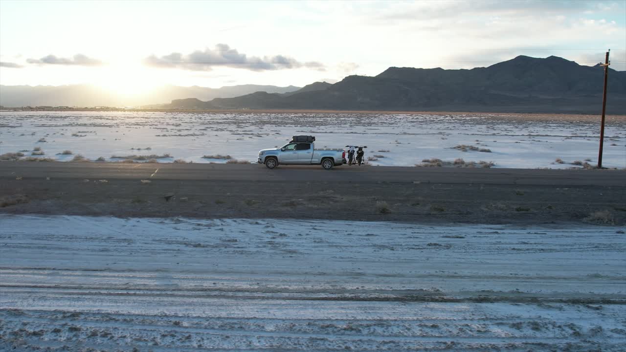 A truck driving down a backroad between the famous Salt Flats of Utah. The sun sets in the background adding to the cinematic vibes of the shot