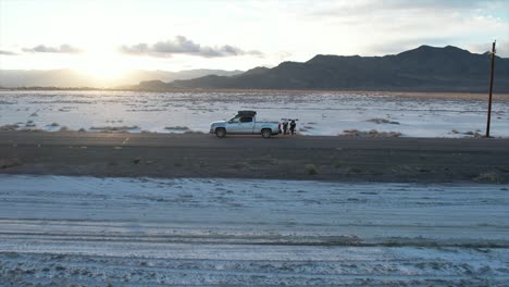 a truck driving down a backroad between the famous salt flats of utah. the sun sets in the background adding to the cinematic vibes of the shot