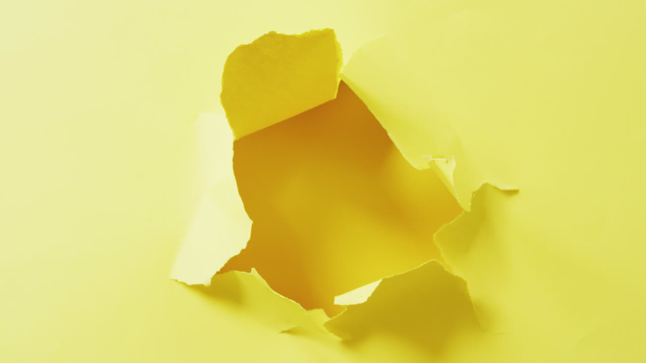 Video in primo piano su un buco strappato in carta gialla su sfondo giallo