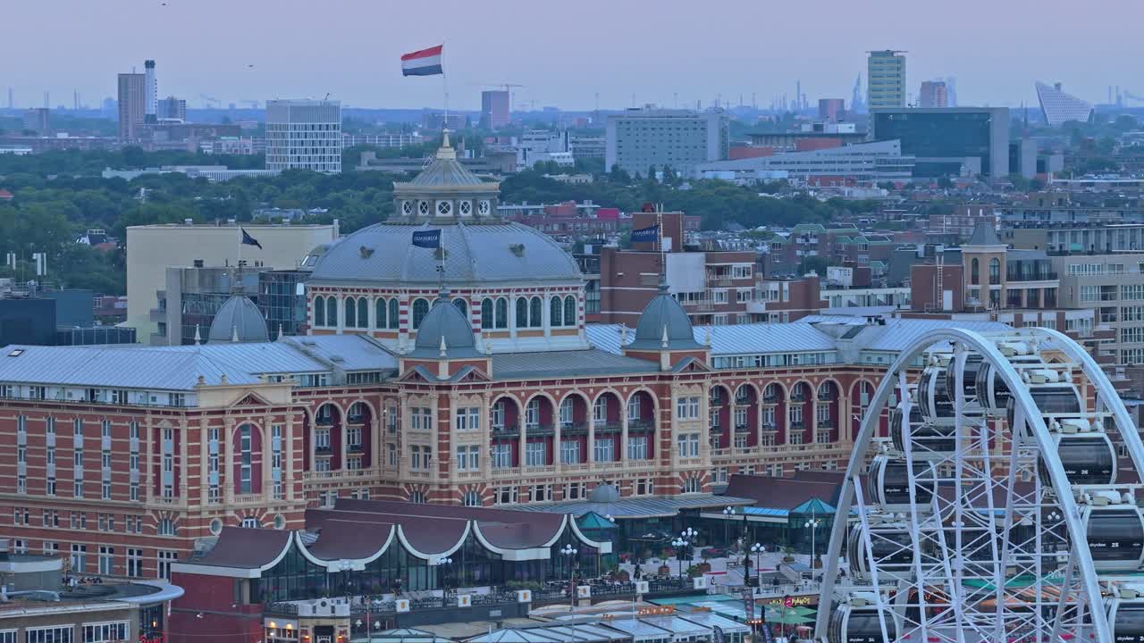 Droneudsigt over Scheveningen Kurhaus hotel ved skumring med vajende hollandsk flag