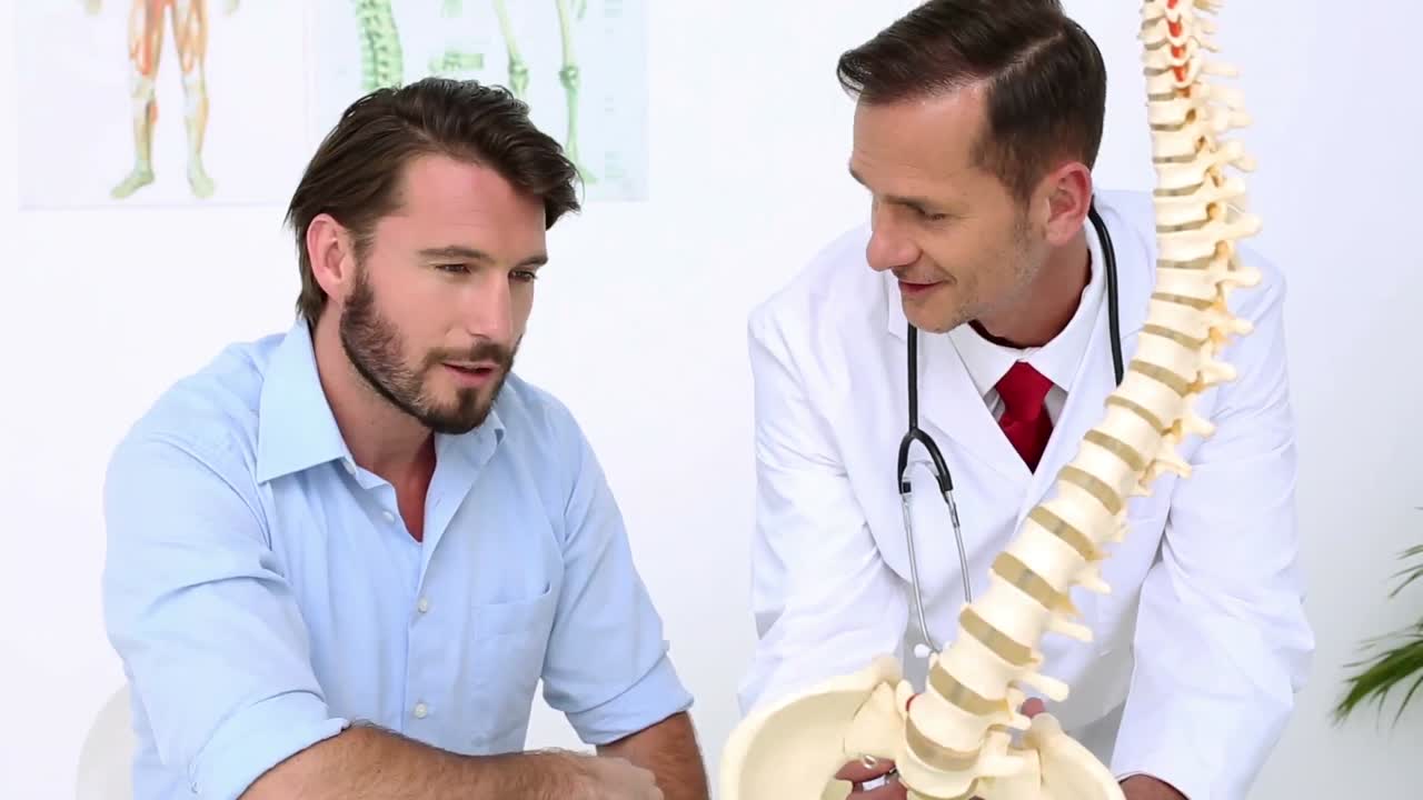 el paciente escucha al médico explicar el modelo de la columna vertebral