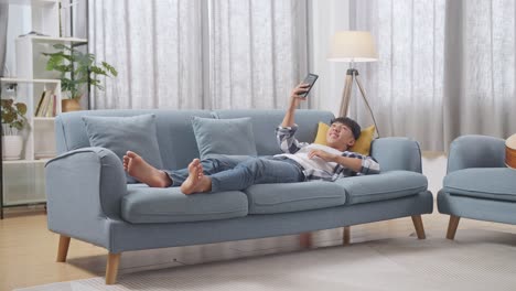 young man relaxing on couch with phone and remote