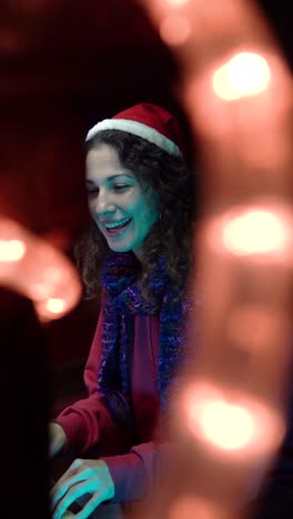 joyful female pianist in a santa hat playing christmas music among festive lights for holiday celebration.